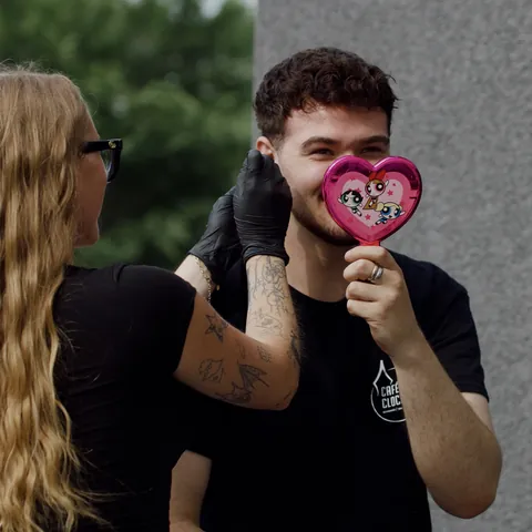 Rox, gloved, at work with a client holding a heart-shaped mirror